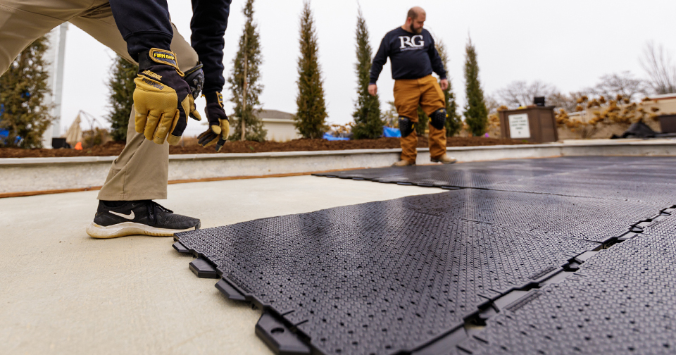 Two Recreational Group team members installing black Ultra Base tiles on concrete bocce court base
