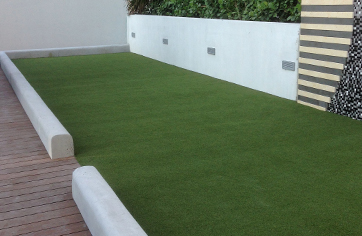 Turf bocce court with concrete border surrounded by decking materials and foliage wall