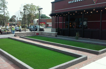 Two turf bocce courts with concrete borders in front of restautrant with outdoor patio