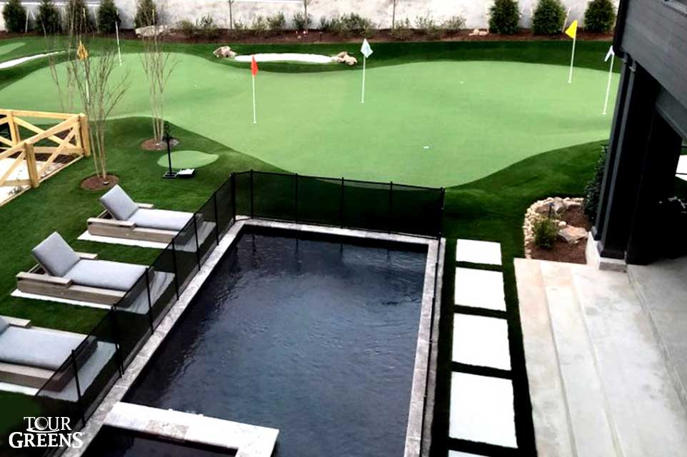 Lakeside backyard pool featuring a poolside short game green