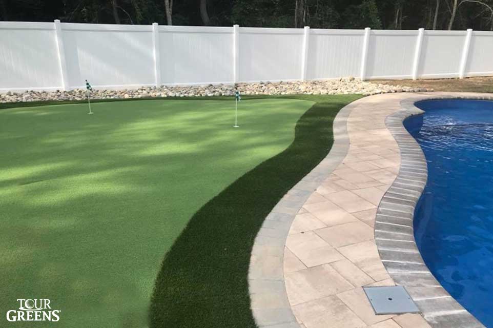 Practice putting green installed next to a backyard pool